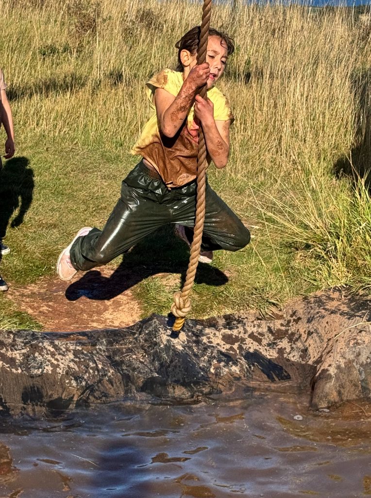 Participant on tarzan rope swing obstacle from muddy pit at Wild Cairns
