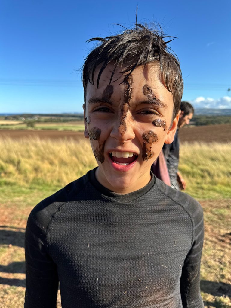 Child covered in mud after completing Wild Cairns assault course obstacle